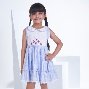 With hand on hips, a little girl stands in a blue striped embroidered collared dress