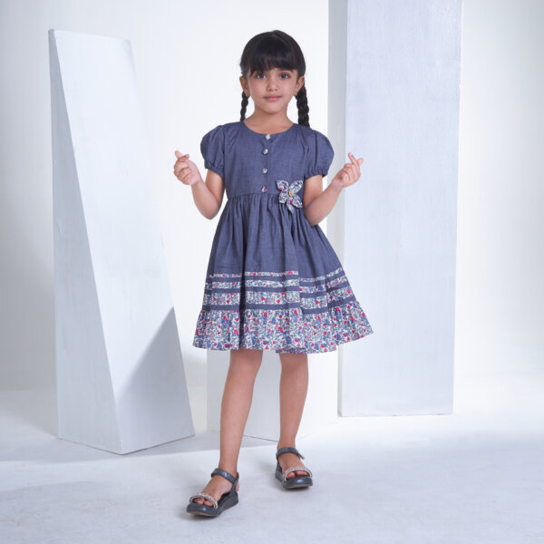Smiling girl in navy flower applique dress with front button fastening, posing confidently