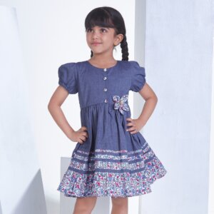With hands on hips, a little girl stands in a navy cotton dress adorned with flower applique