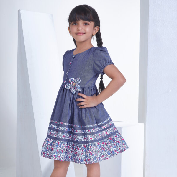 Posing from the side, a little one wears a navy cotton dress adorned with flower applique