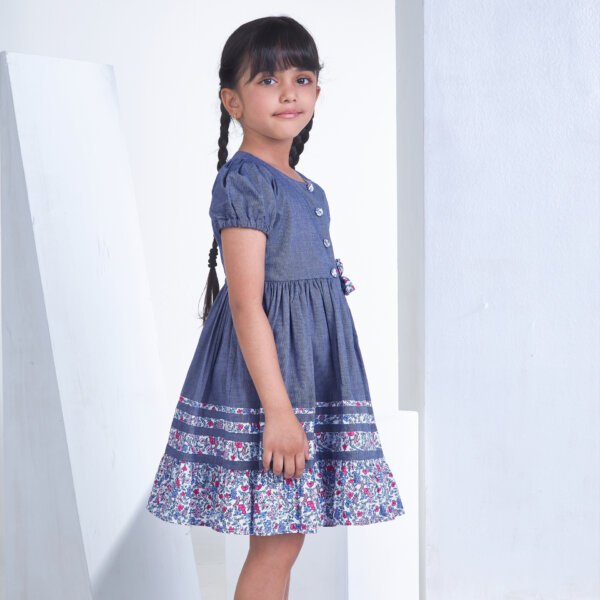 Posing from the side, a little one wears a navy cotton dress adorned with flower applique