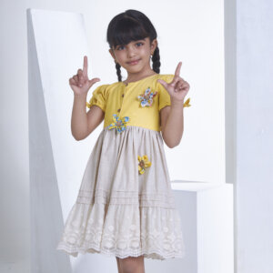 With a cute pose, a little one wears a yellow flower applique dress adorned with lace
