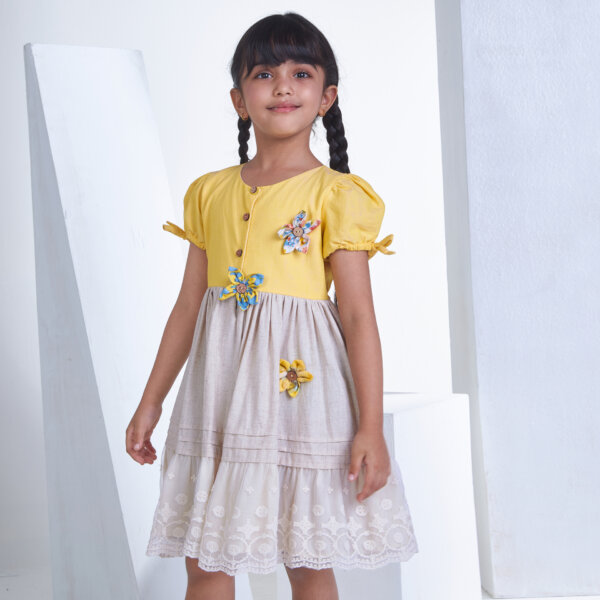 Posing from the side, a little one wears a yellow flower applique dress adorned with lace