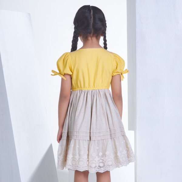 A girl seen from behind wearing yellow flower applique dress with elasticated waist