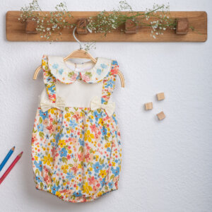 An Ivory hand-embroidered floral printed baby girl onesie hanging on a hanger.