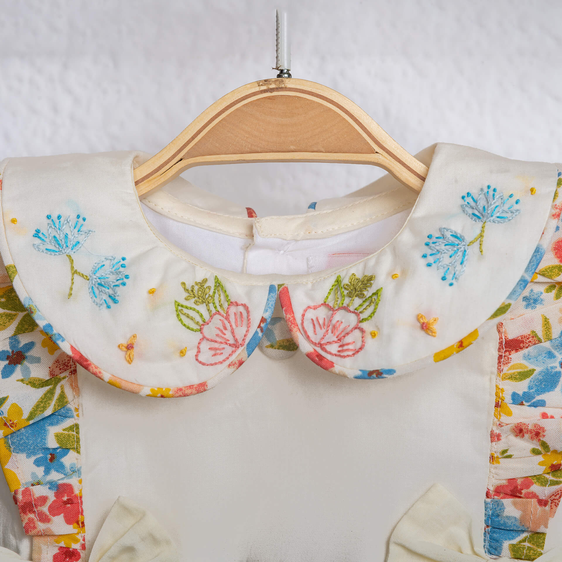 Close-up of hand embroidery detail on an ivory floral printed baby girl onesie from Soleilclo.